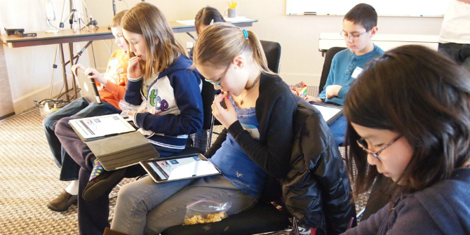 children sitting side by side looking at digital devices