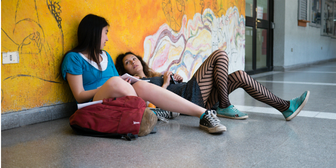 two girls sitting on floor looking at each other with their backs against a wall