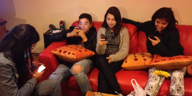 2 kids sitting on couch looking at their smartphones