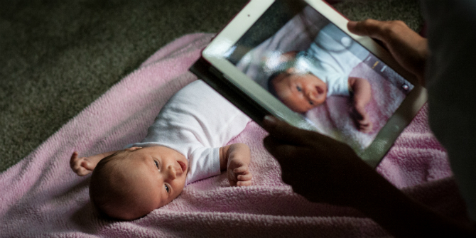 baby laying on back while someone takes a photo on an ipad 