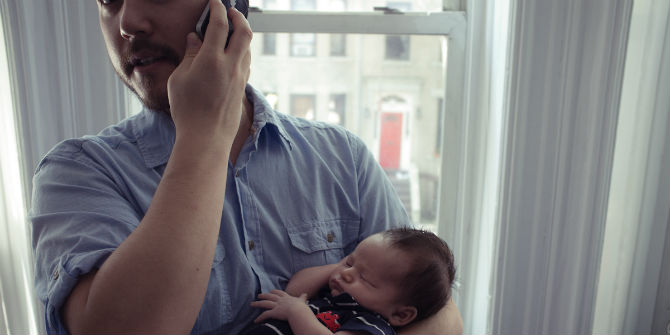 Man holding baby while also holding cell phone to his ear.