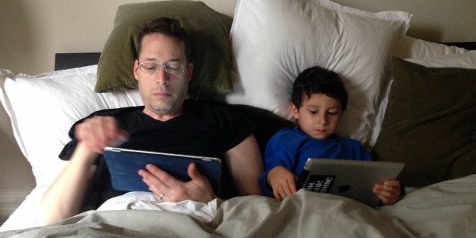 dad and son lying in bed next to each other looking at tablet screens